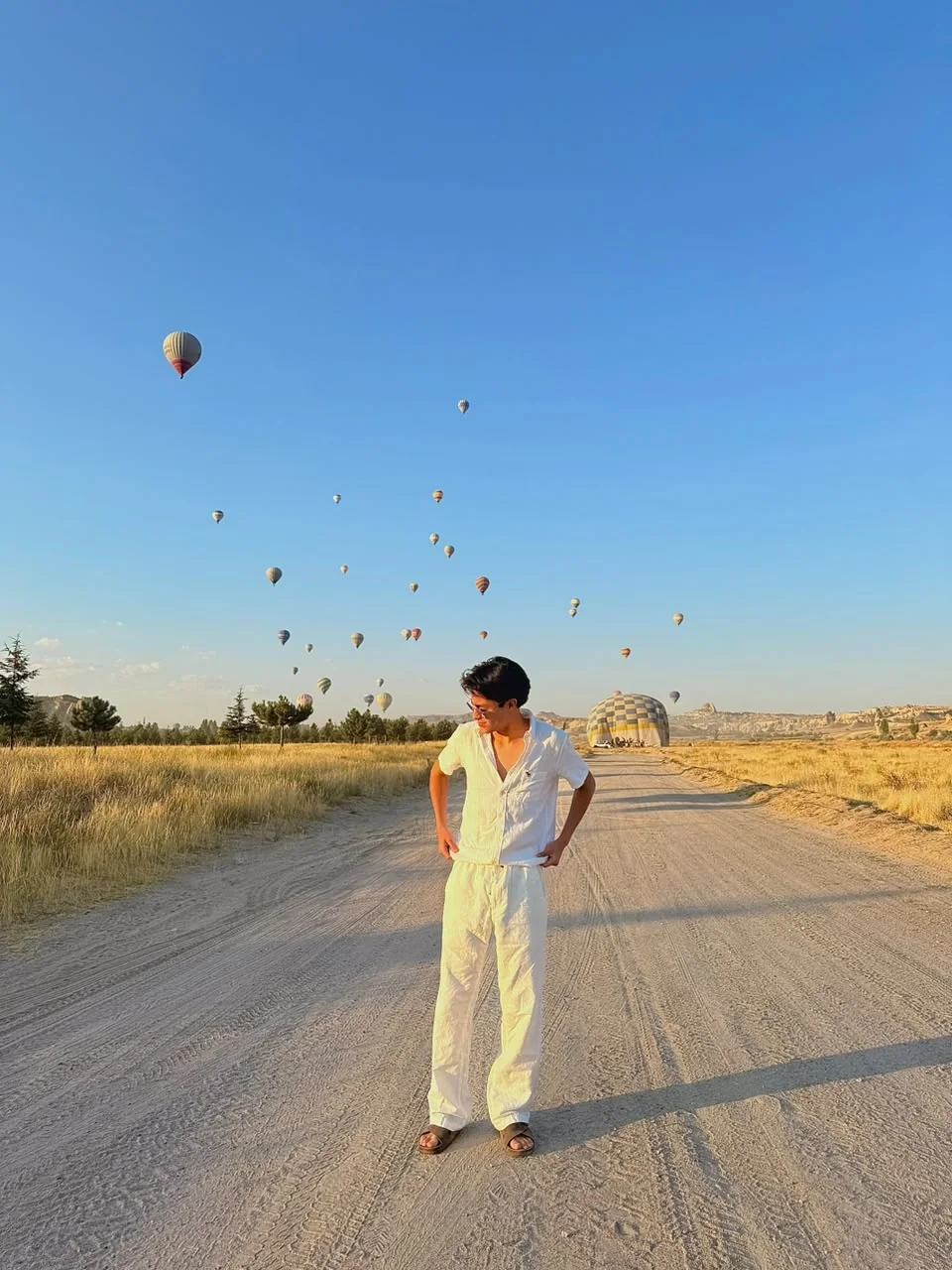 Viajero de pie en un camino de tierra de Capadocia con una veintena de globos elevándose al fondo