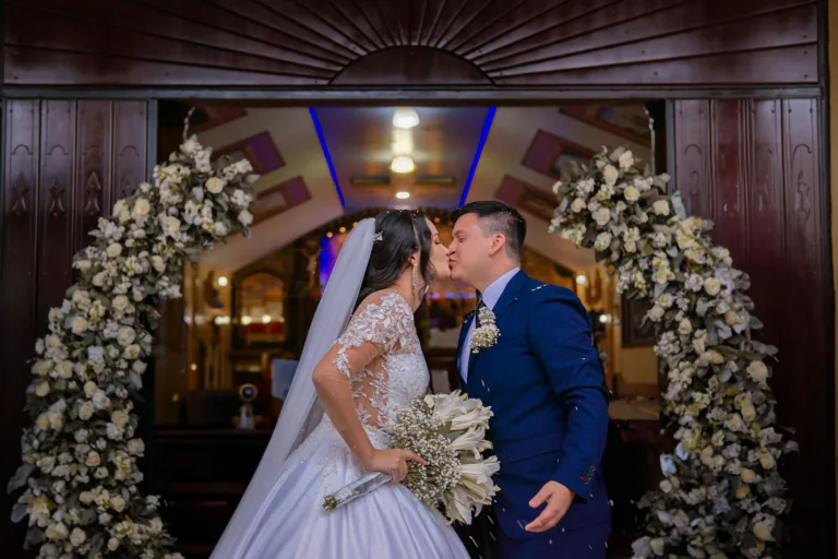 A couple shares a kiss beneath floral arch during a wedding in Santo Domingo de los Tsáchilas, Ecuador.